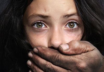 A close-up of a person's face with a dirt-stained hand covering their mouth, capturing a fearful and intense expression.