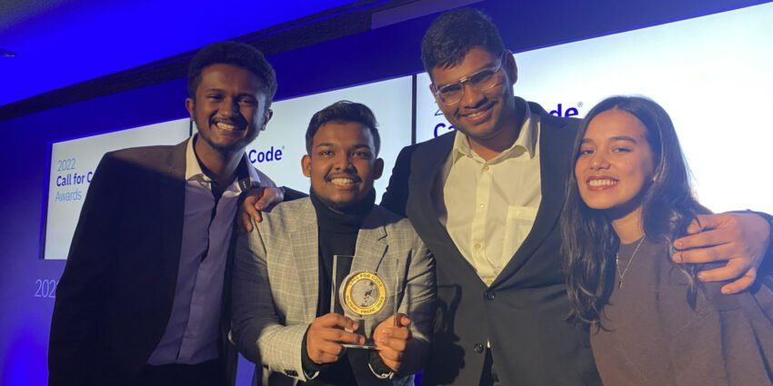 Four smiling individuals standing together on a stage at an awards ceremony, with one person holding a circular trophy.