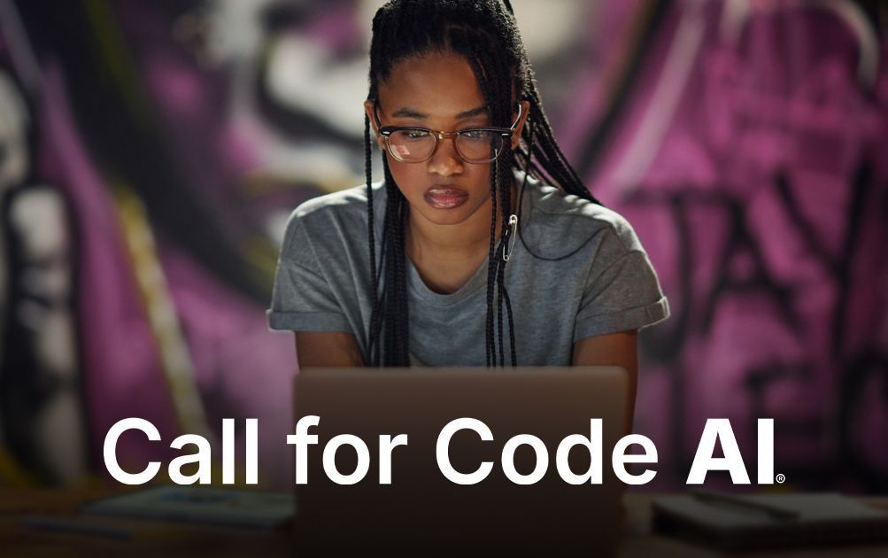 A focused person in glasses works at a laptop in front of a purple graffiti wall, with the text 