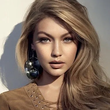 Portrait of a woman with blonde hair, wearing large circular metallic earrings and a brown top with stud details.