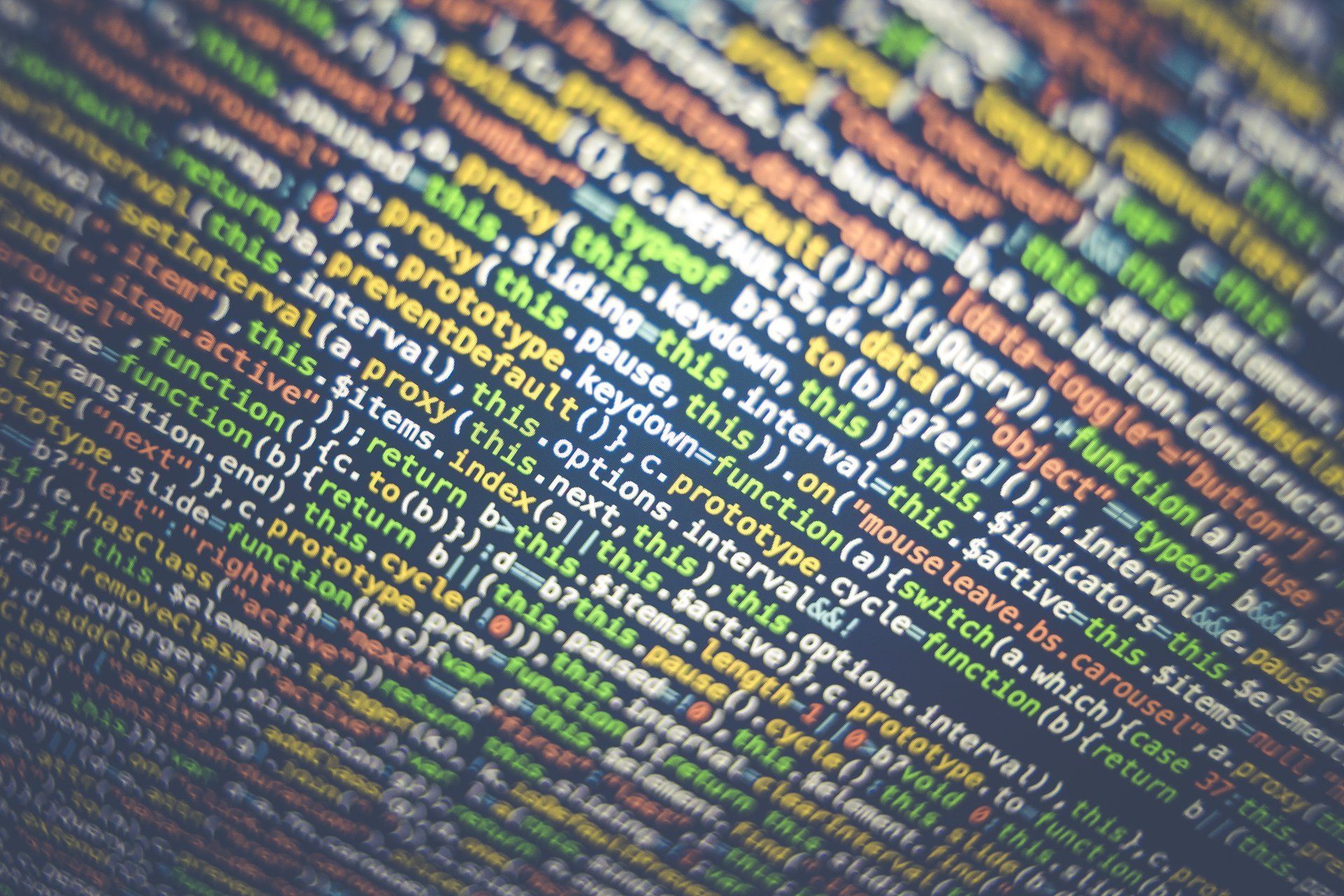 Close-up, blurry view of colorful JavaScript code on a computer screen, with text syntax highlighted in various colors.