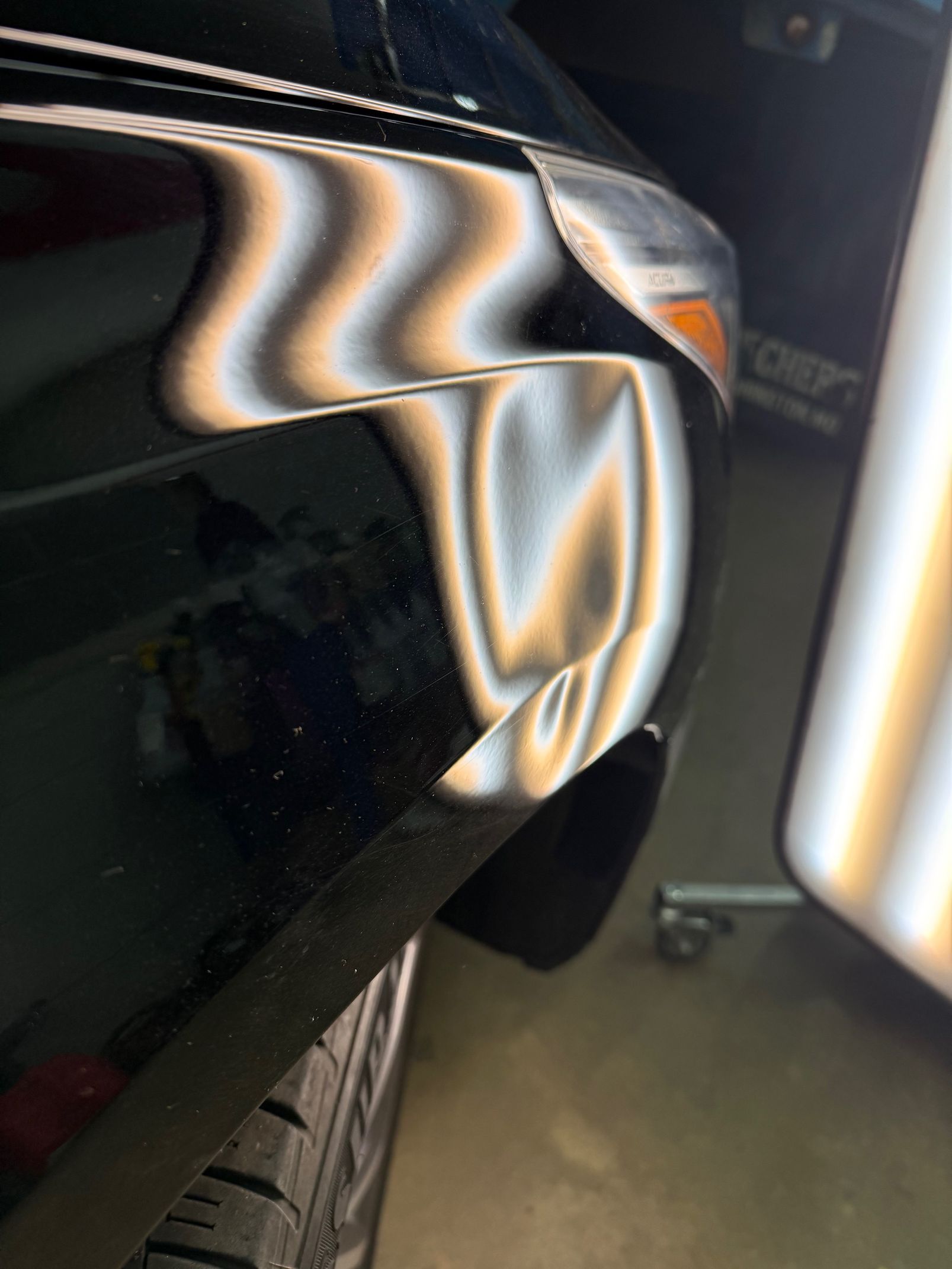 Black car fender with reflective bodywork and visible front tire in a garage or workshop
