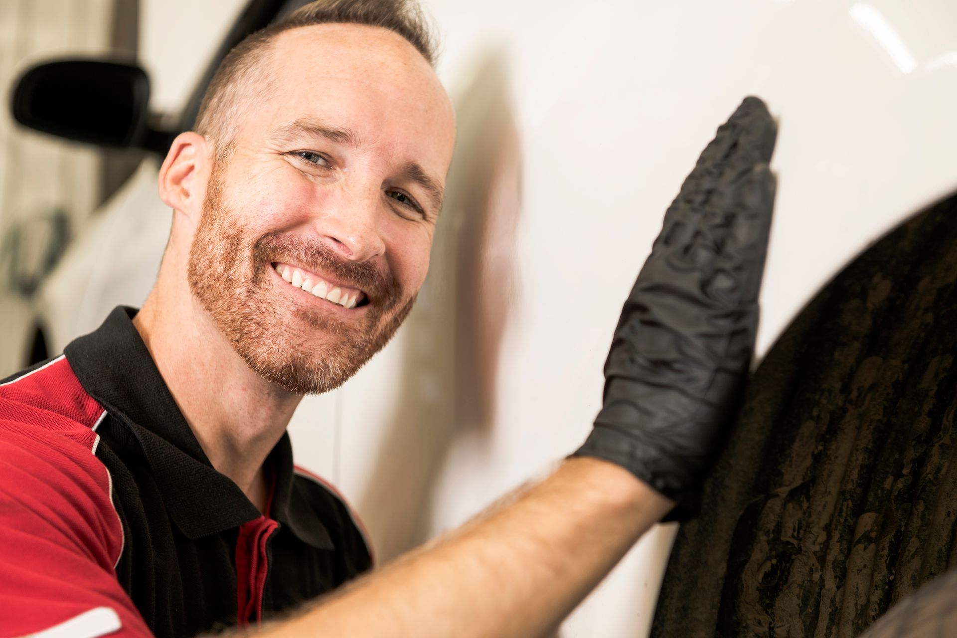 Smiling person in a red shirt and black glove wiping a dark surface indoors