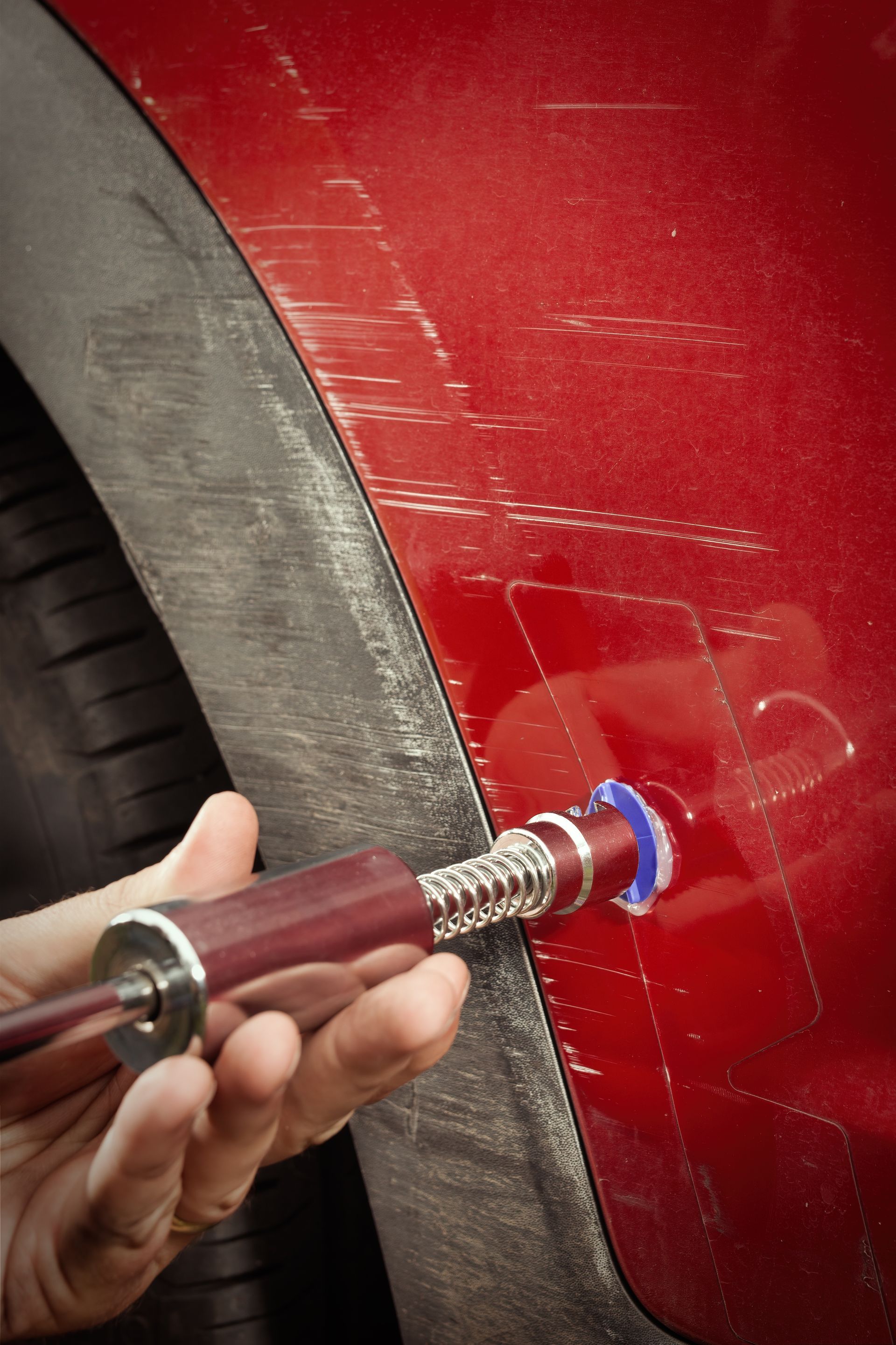 Handheld tool polishing a red car panel near the wheel arch
