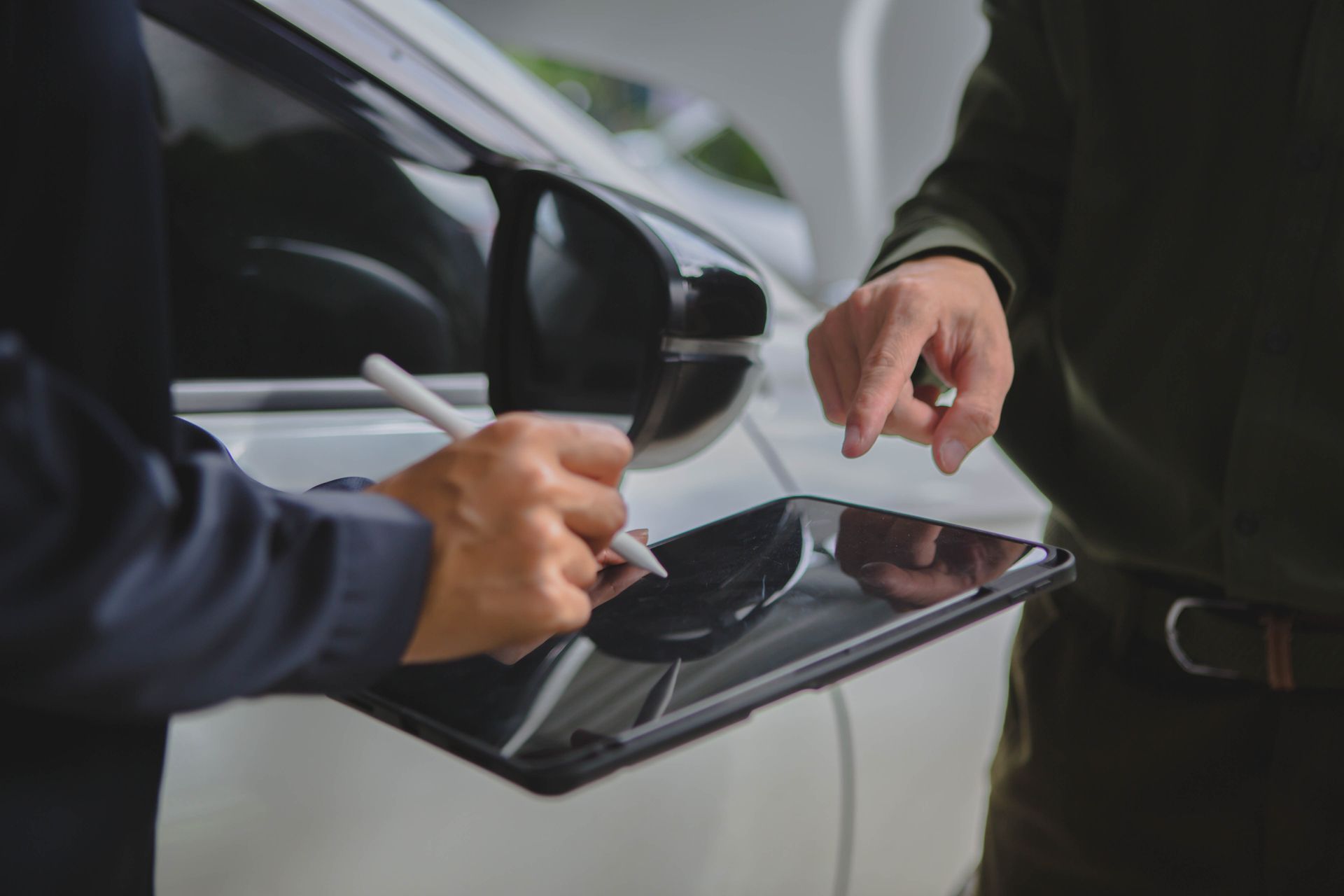 Two people signing documents on a tablet beside a white car