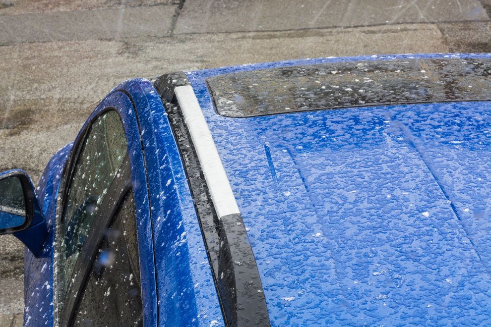 Blue car roof and windshield covered in hail or heavy rain, parked outdoors.