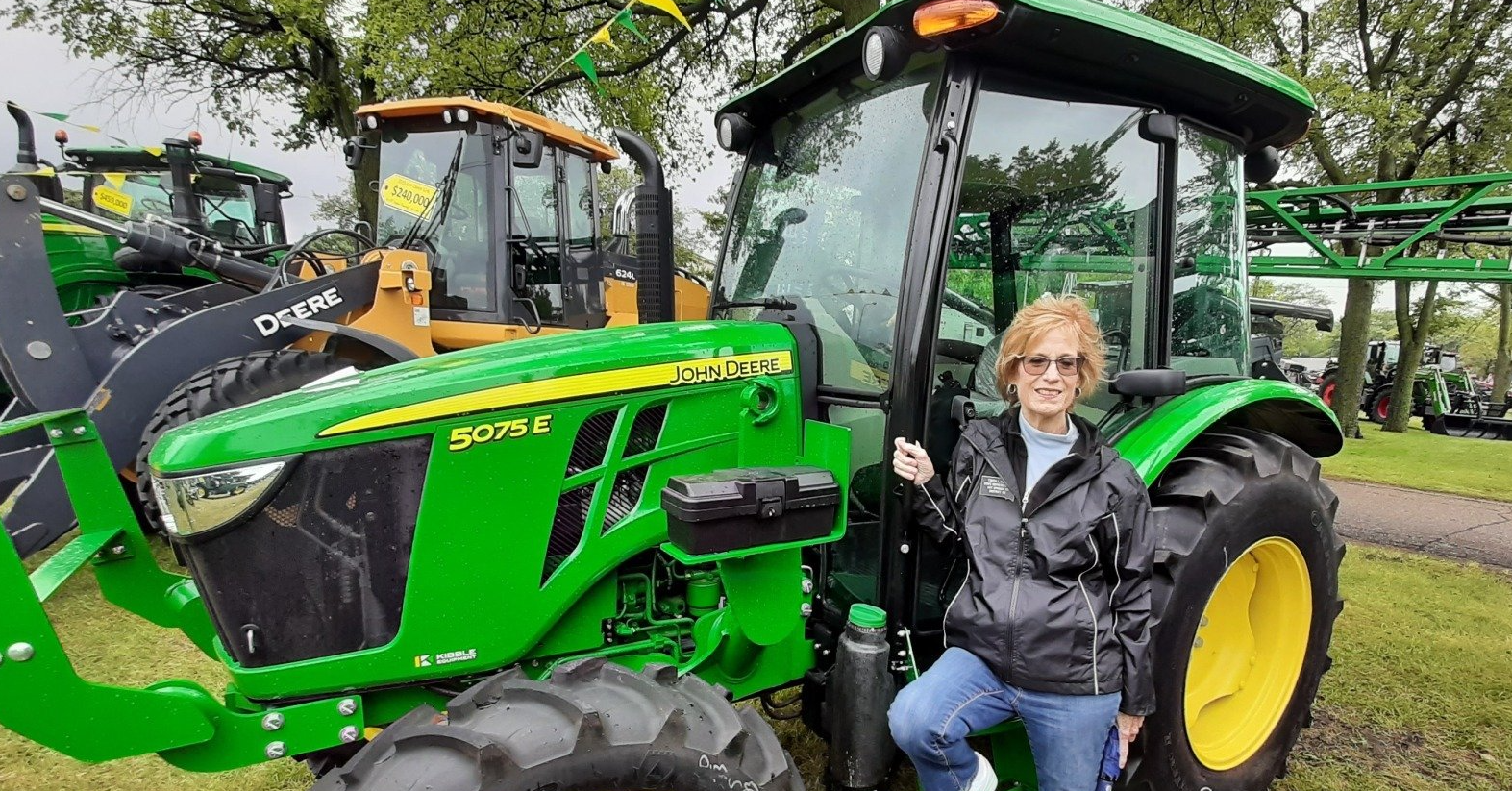 Trish standing beside a green and yellow John Deere tractor outdoors. 