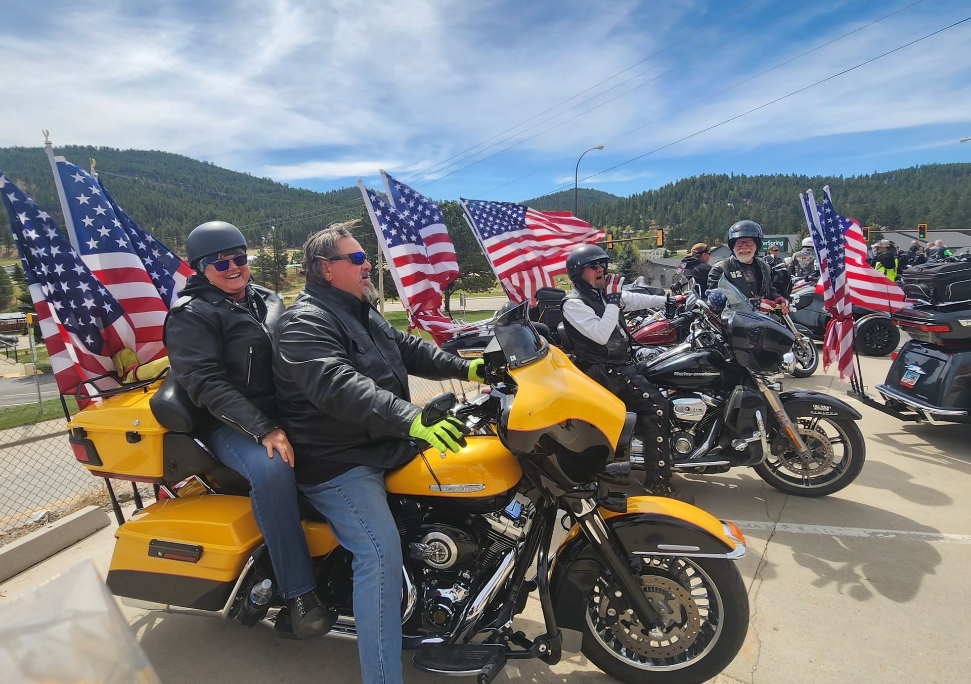 Motorcyclists with American flags riding through a mountain road parade, led by a yellow bike