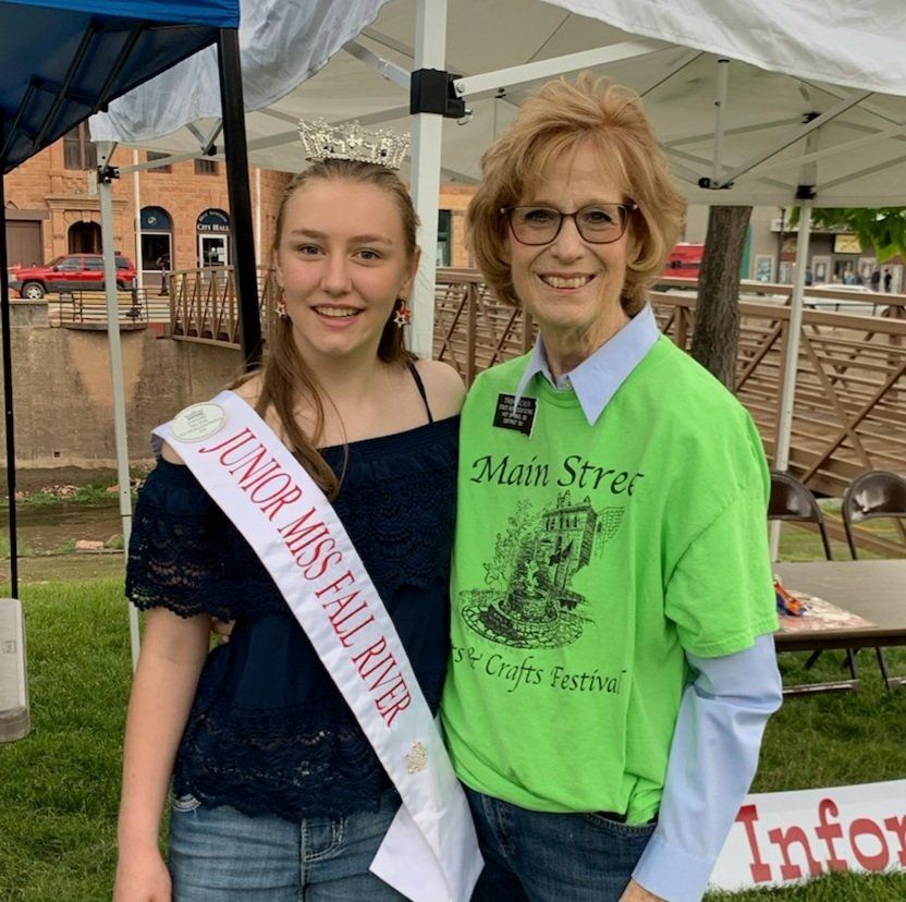 Junior Miss Fall River poses with a woman at a festival information booth, both smiling.