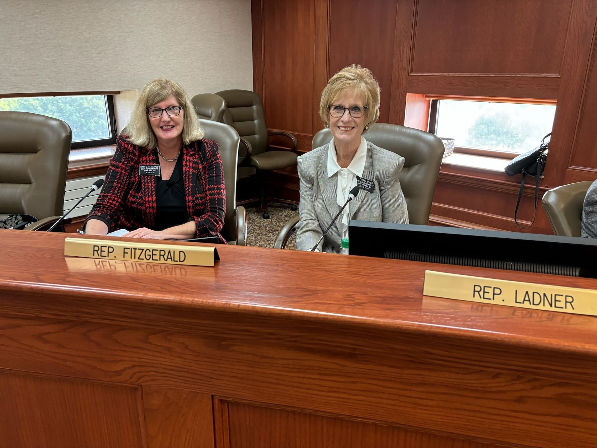 Trish and Mary Fitzgearld seated behind nameplates at a council-style dais in a wood-paneled room
