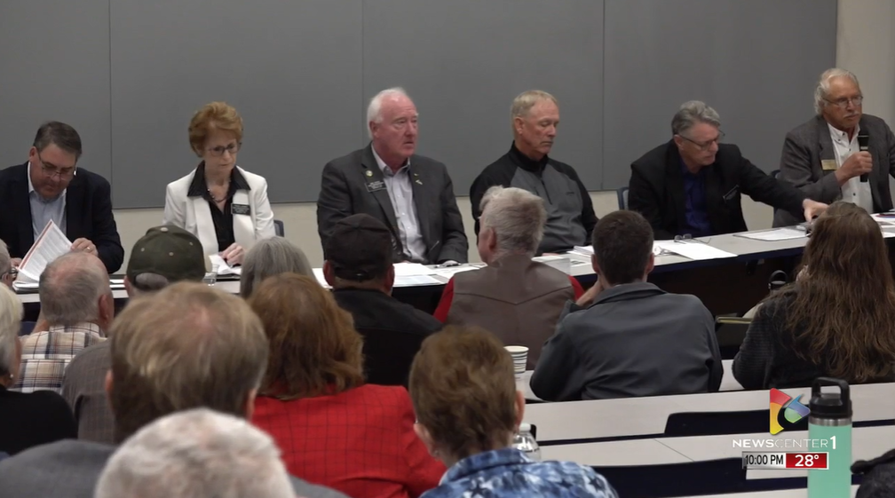 Panel of people seated at a table, speaking to an audience in a room.