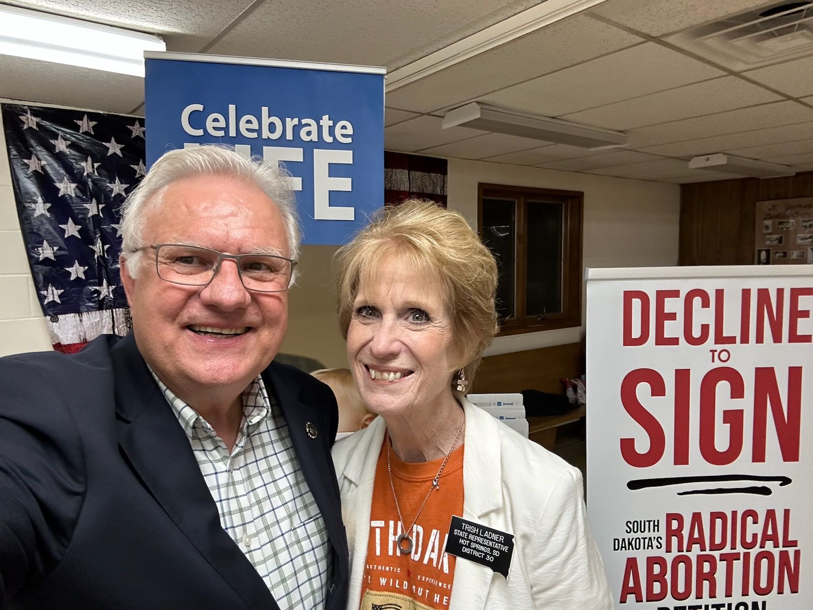 Man and woman smiling, near signs that say 