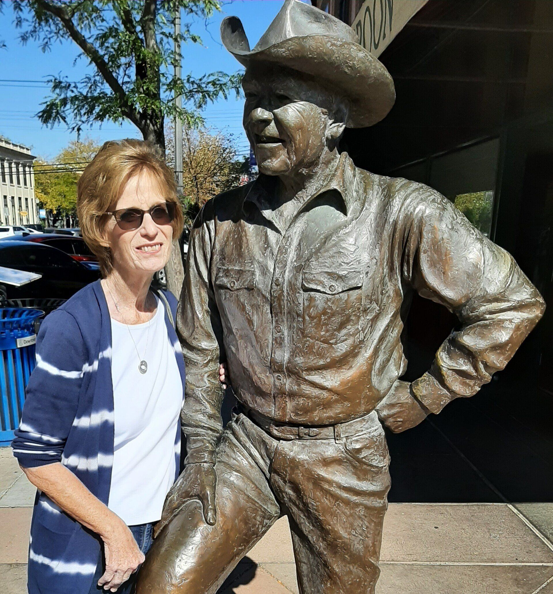 Woman stands next to a bronze statue of a man wearing a cowboy hat.