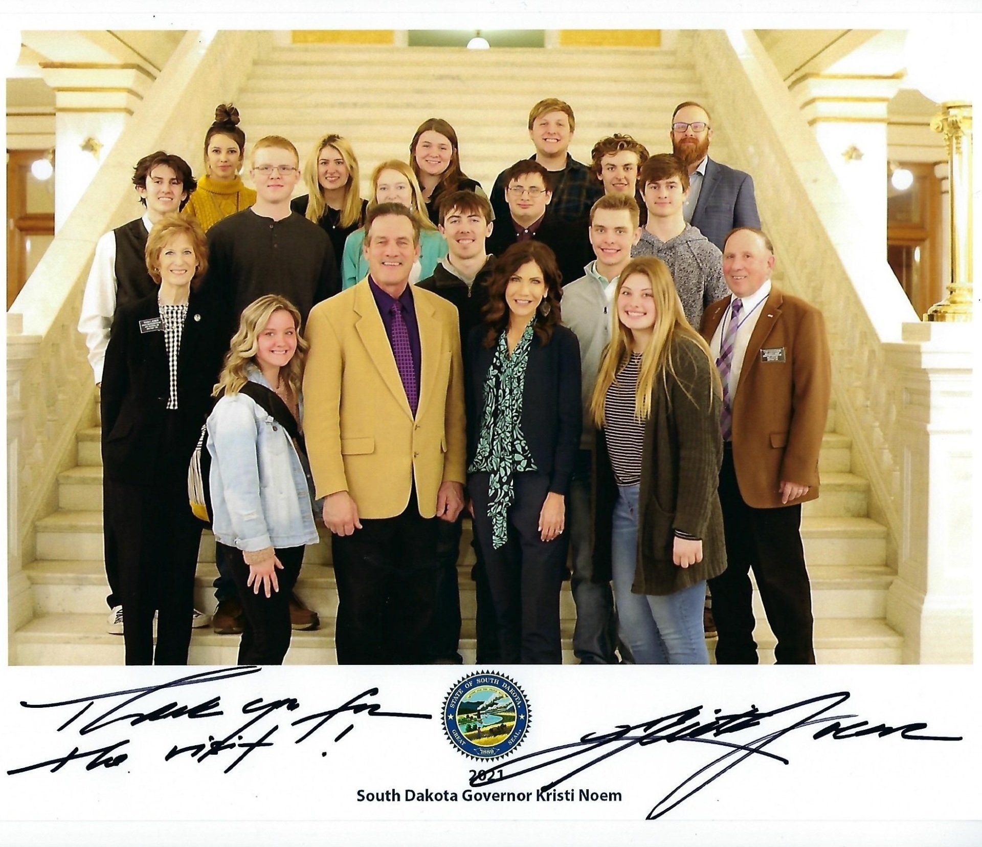 Group photo on stairs with two men and woman in the middle; autograph at the bottom.