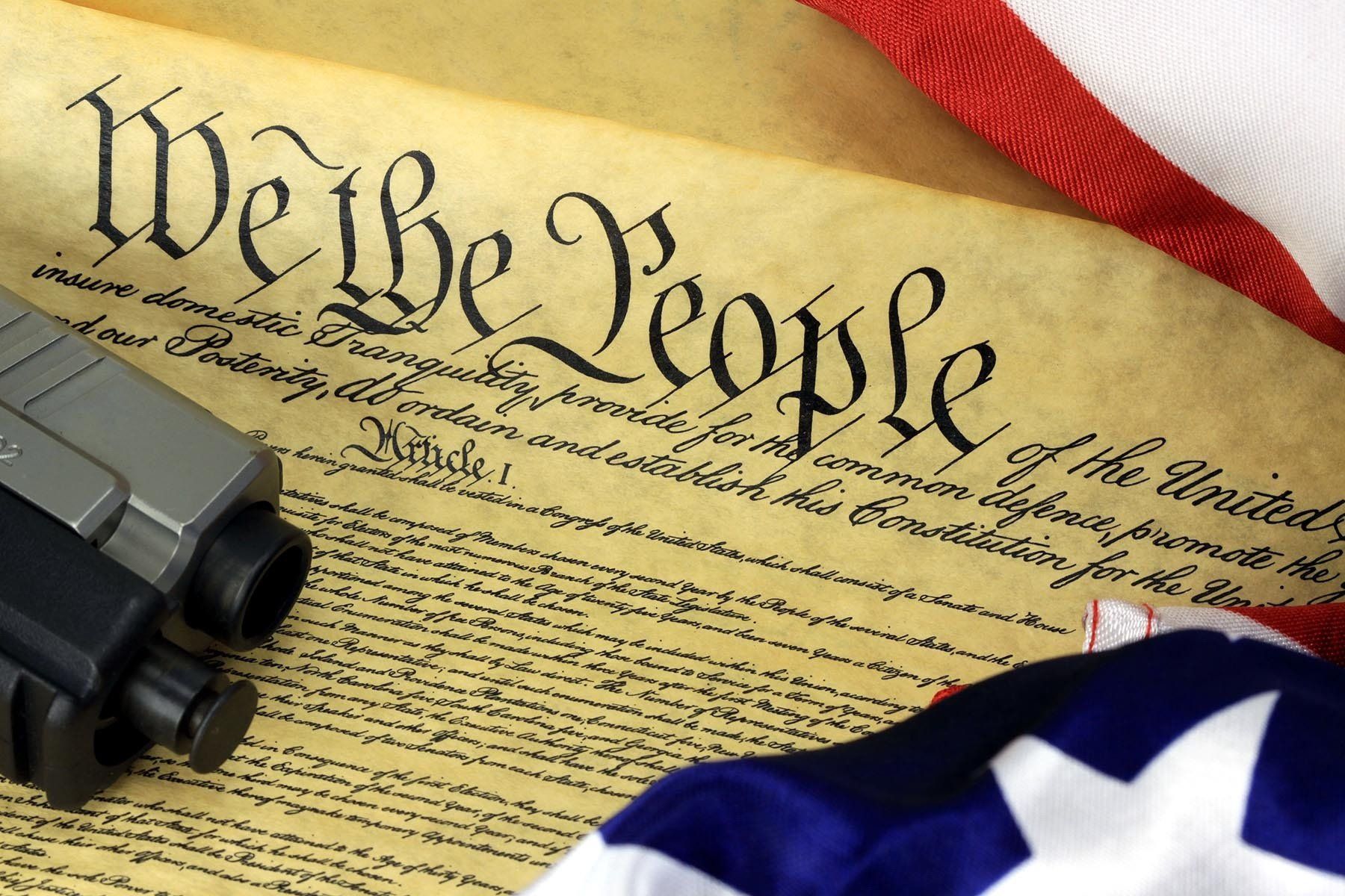 U.S. Constitution document with a gun and American flag draped over it.