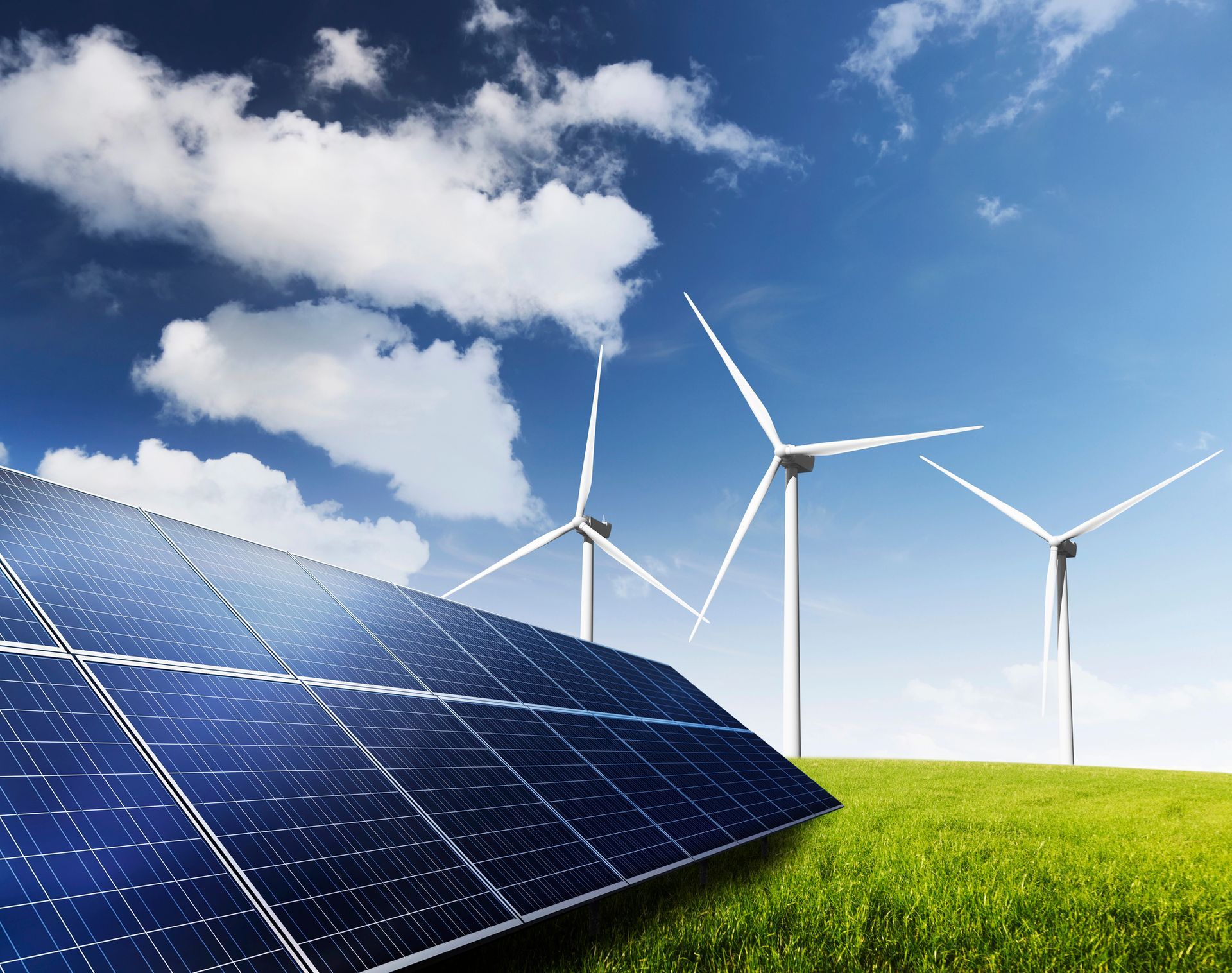 Pannelli solari in un campo verde con turbine eoliche sullo sfondo di un cielo azzurro con nuvole.