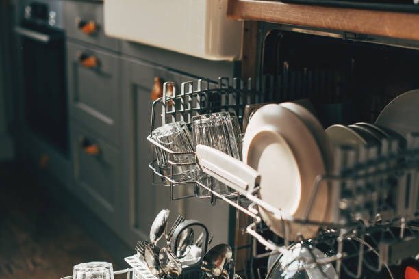 A dishwasher is filled with plates , cups , and silverware in a kitchen.