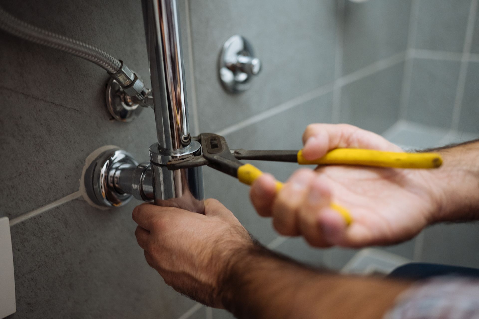 A man is fixing a pipe with a wrench in a bathroom.