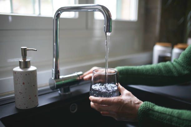 A person is pouring water into a glass in a kitchen sink.