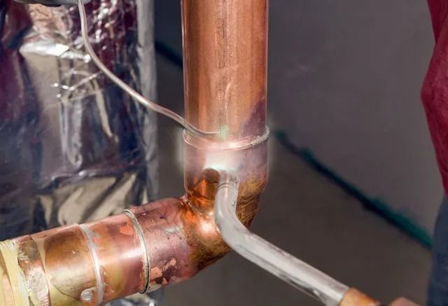 A person is welding a copper pipe with a soldering iron.