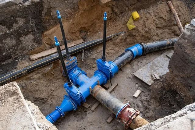A bunch of pipes are laying in the dirt in a trench.