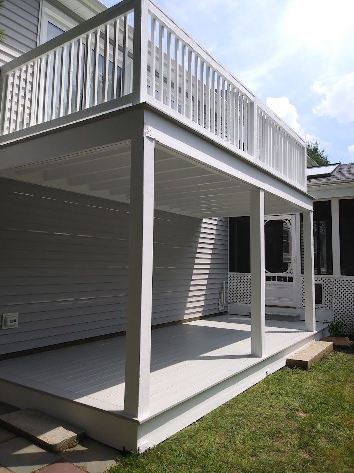 White two-story porch or deck with railings and support posts beside a house, overlooking a grassy yard