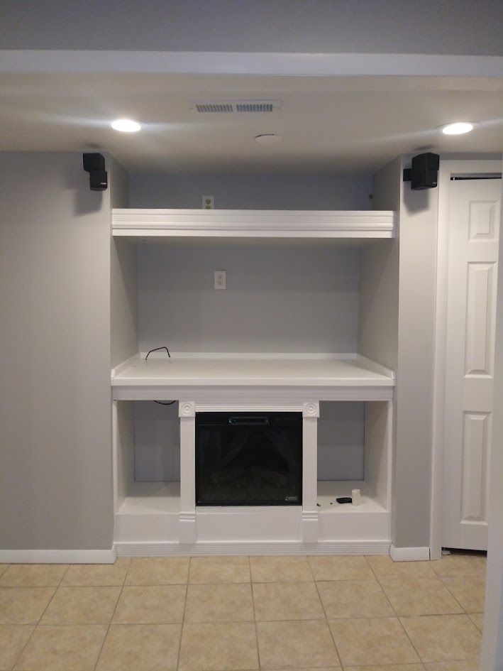 Built-in white entertainment center with shelves and black fireplace insert in a tiled room.