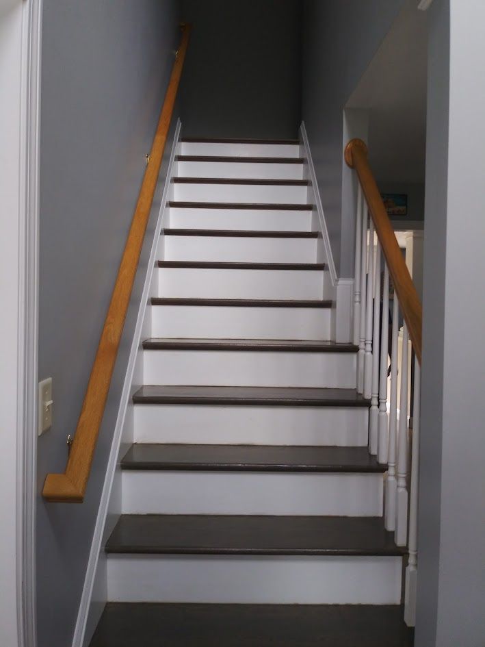 Indoor staircase with white steps, gray walls, and wooden handrails on both sides