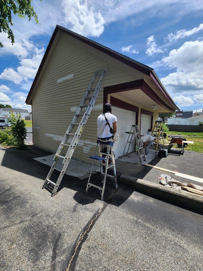 Worker on ladder painting a house exterior under a bright blue sky