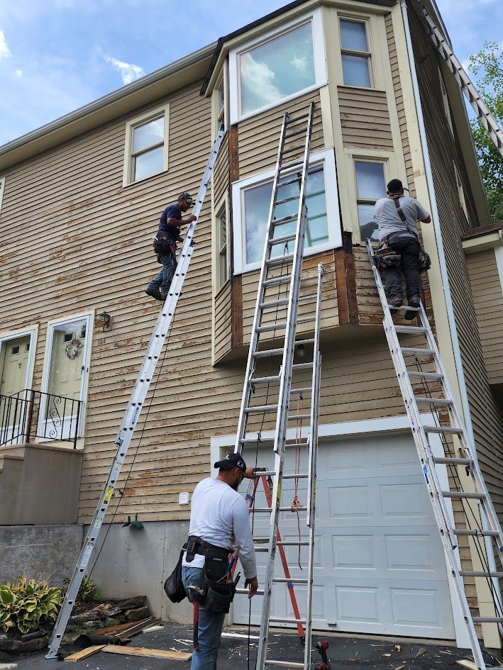 Workers on ladders repairing the exterior of a two-story house above a garage.