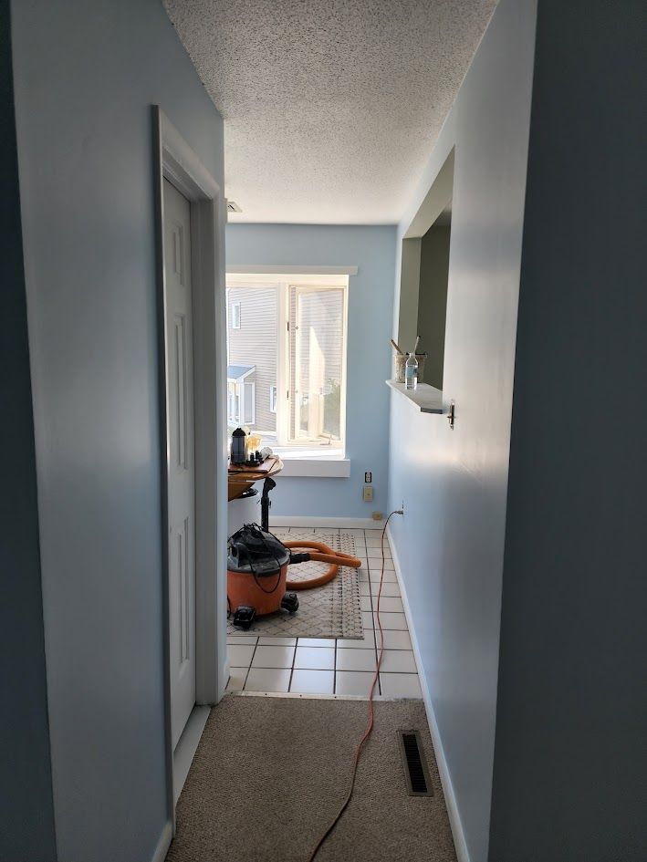 Narrow hallway under renovation with tools, unfinished tile floor, and a window at the end