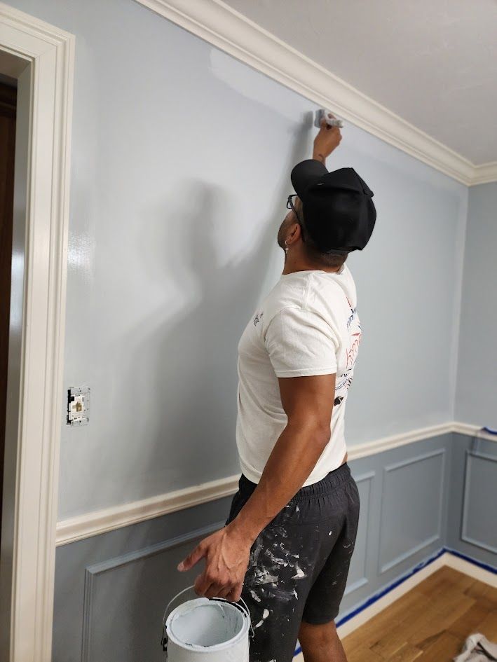 Painter touching up trim on a light blue wall in a room with white molding and wood floors