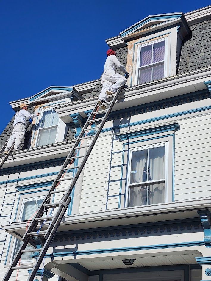 Workers on ladders repairing the roof of a blue house under a clear sky