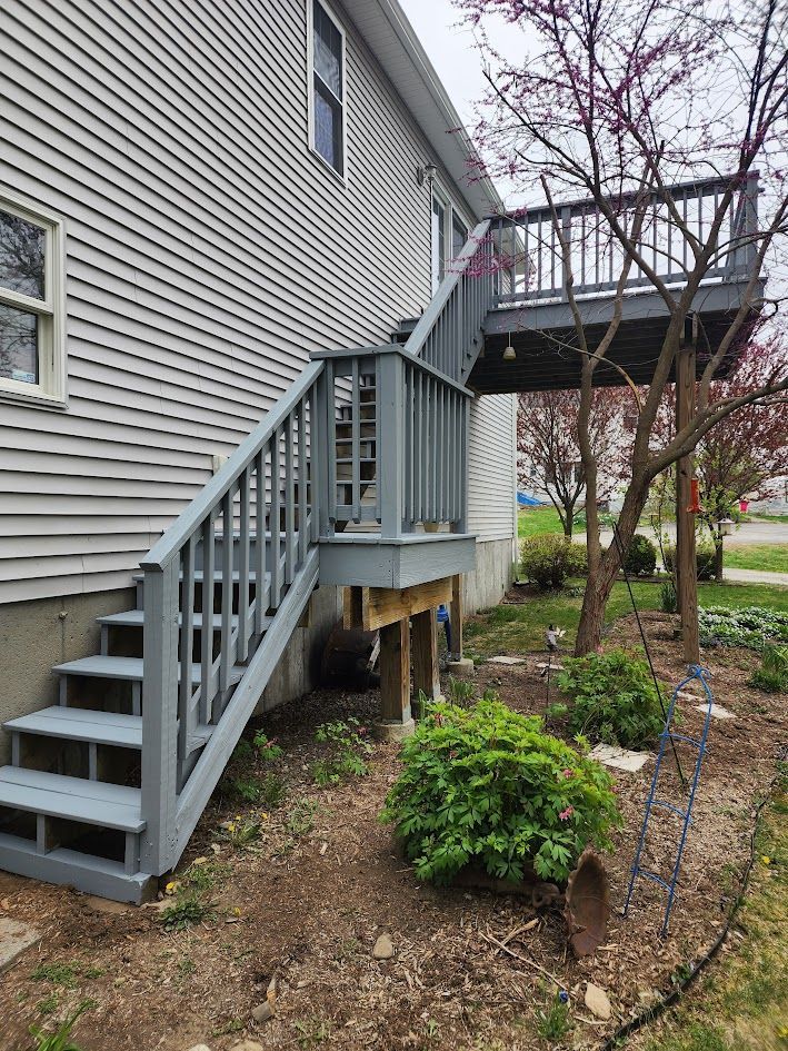 Backyard exterior with gray house, wooden stairs, elevated deck, and landscaped garden beds