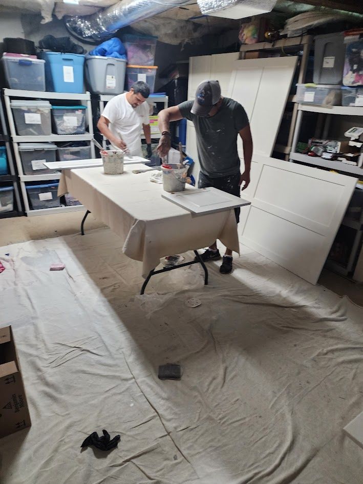 Two people assembling a white table in a cluttered basement workshop