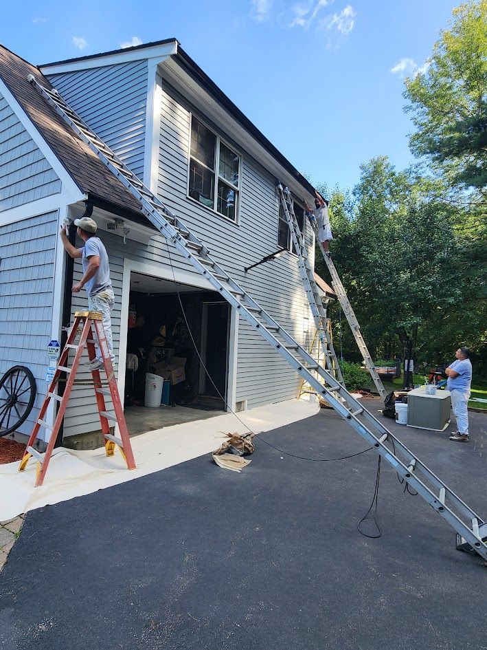 Workers on ladders repairing a two-story house exterior with white siding and a black driveway