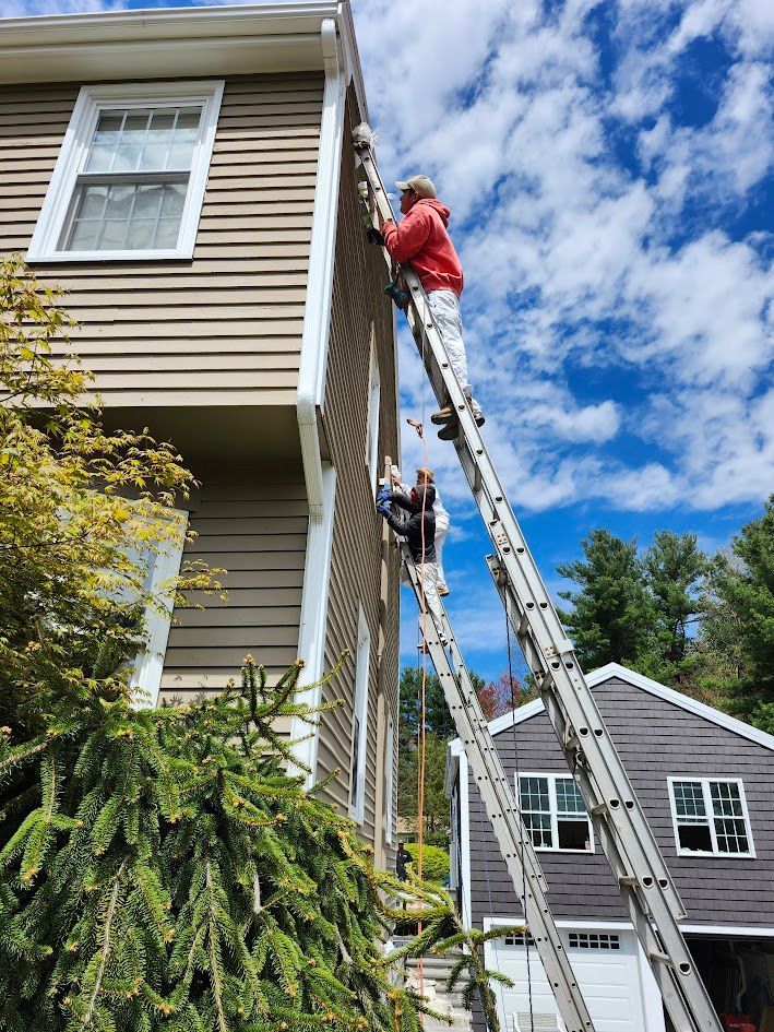 Workers on ladders painting a beige house exterior under a blue sky