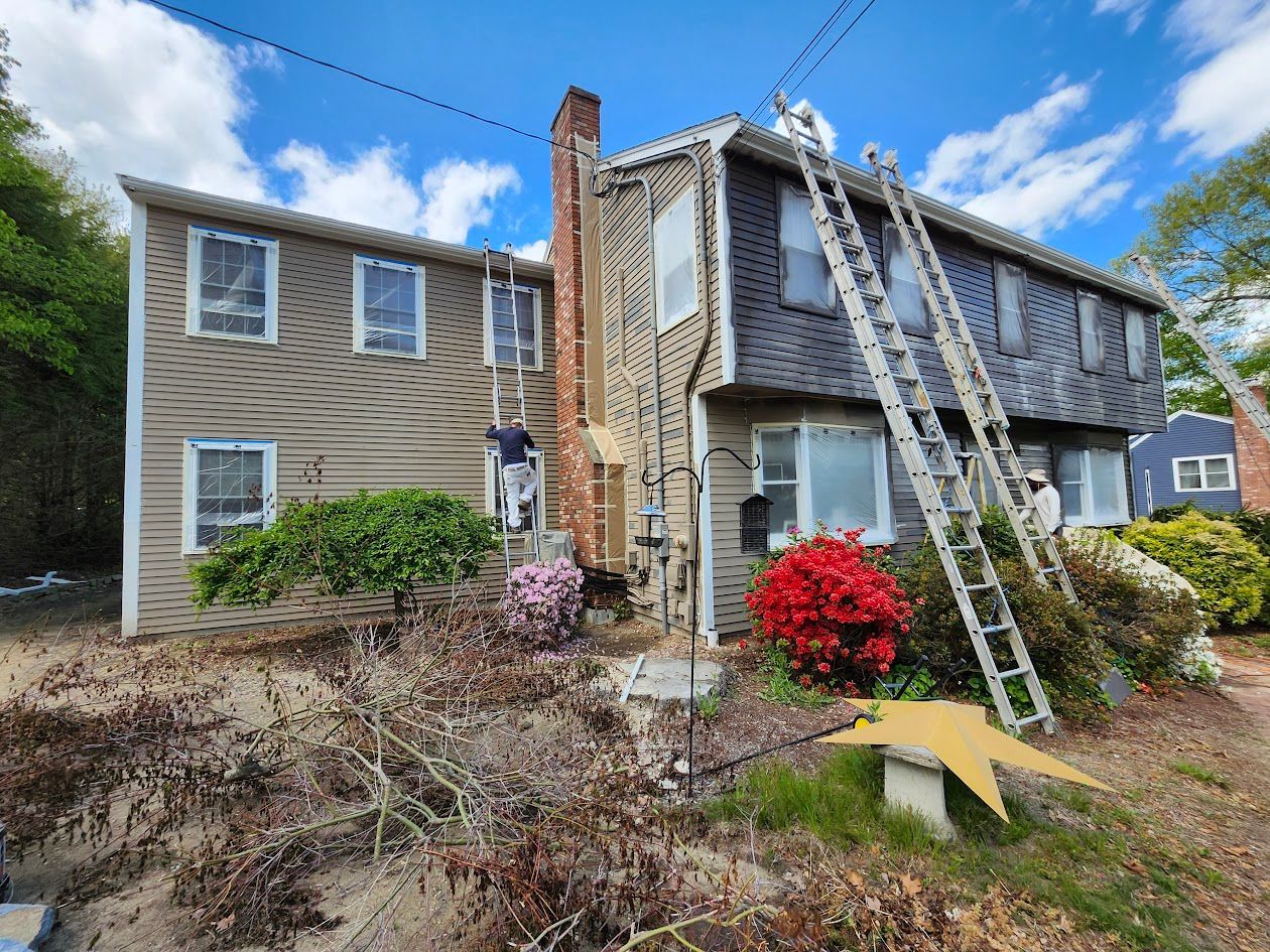 Two-story house with ladders leaning against the roof and chimney, suggesting exterior repair work