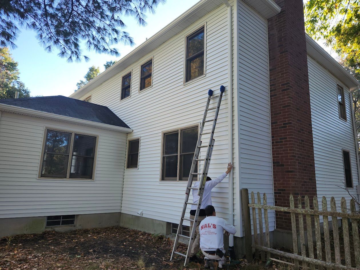Workers painting a white two-story house with a ladder and paint bucket