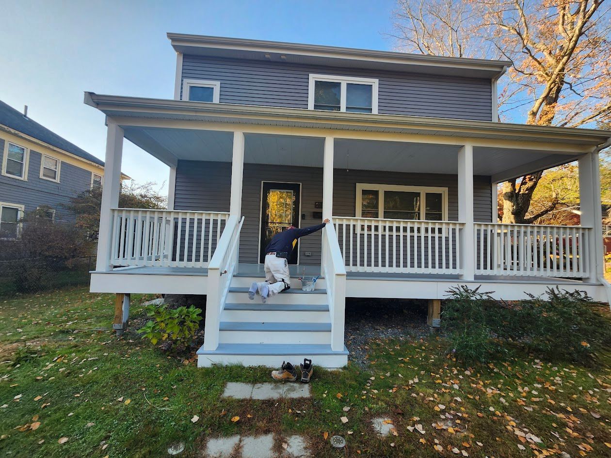 Front porch of a gray house with white railings and steps, with a small dog sitting on the steps.