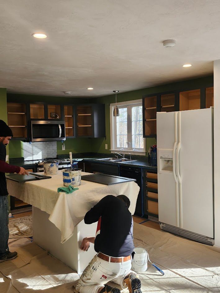 Two people installing a kitchen island in a dark-wood kitchen, with tools and supplies on the counter.