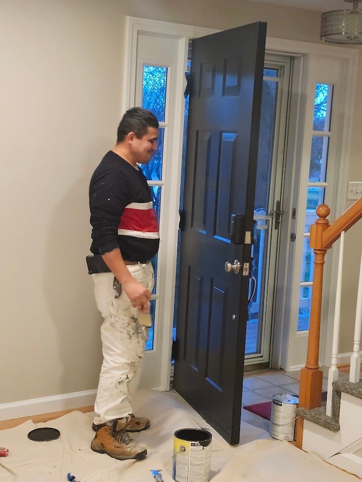 Man standing by an open black front door in a foyer with paint supplies on the floor