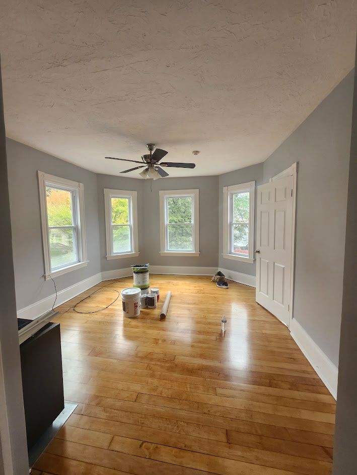 Empty living room with gray walls, hardwood floors, windows, ceiling fan, and white closet doors