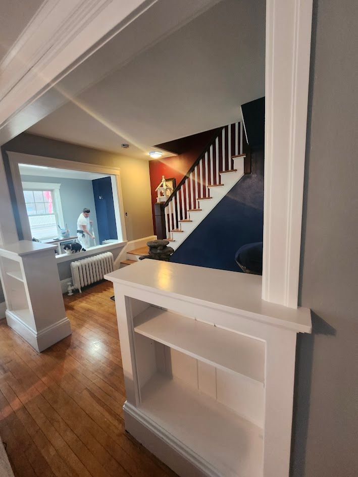 Interior hallway with white trim, hardwood floor, staircase, and a window seat in a bright home.