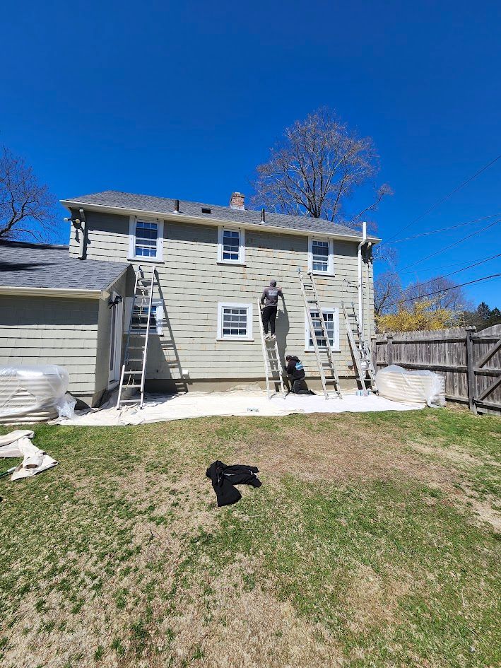 Two workers on ladders painting a two-story beige house on a sunny day