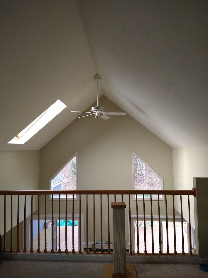 Loft interior with vaulted ceiling, ceiling fan, skylights, and railing overlooking a lower level