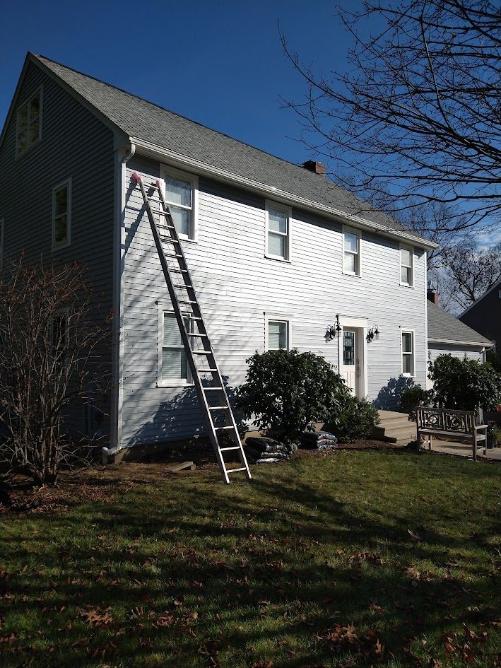 Two-story white house with a ladder leaning against the siding under a clear blue sky