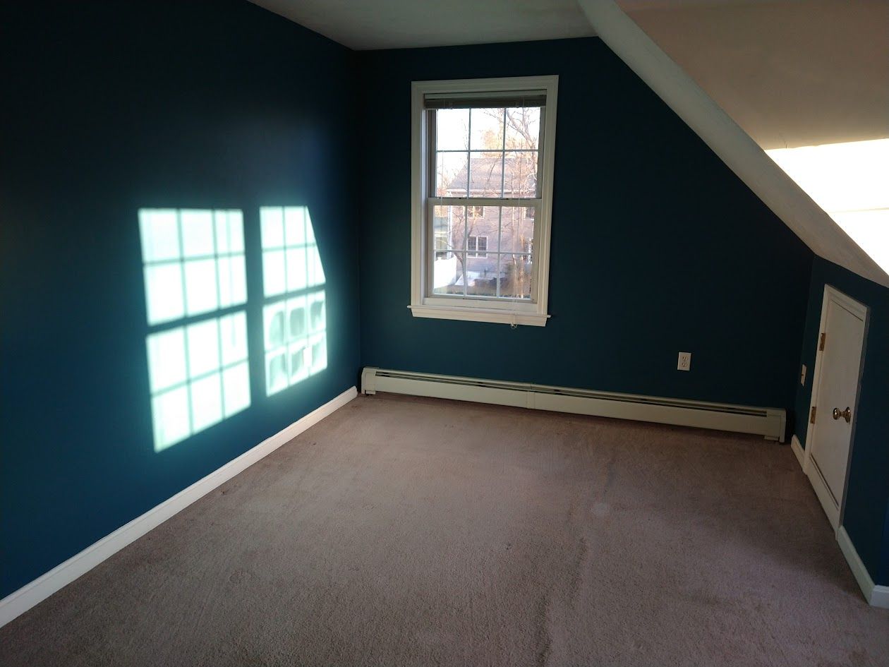 Empty carpeted room with teal walls, a window, and a sloped ceiling.