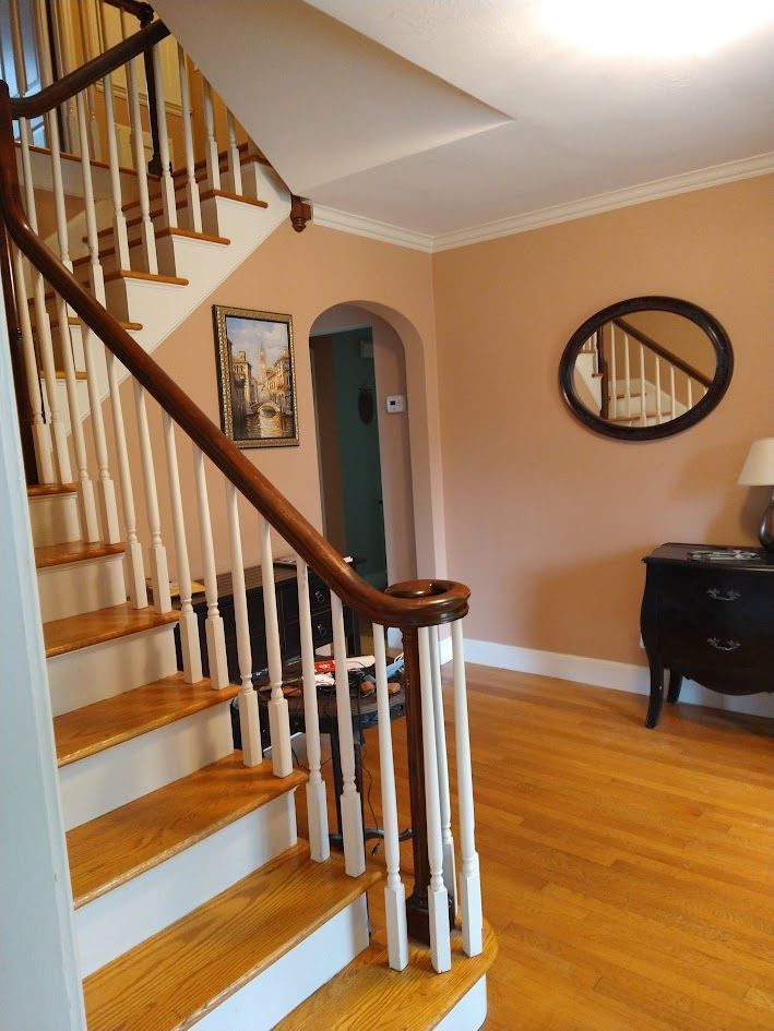 Staircase with wood banister in a peach-painted foyer, with a round mirror and small table on hardwood floor