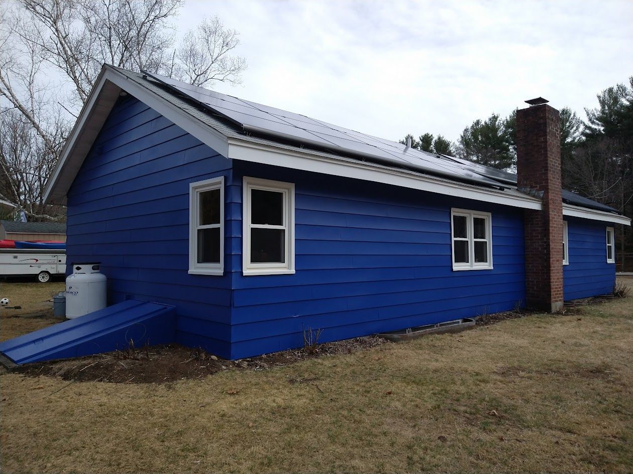 Blue house with white trim and a ramp, viewed from the side on a grassy lot.